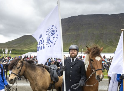 Frá Landsmóti hestamanna á Hólum í Hjaltadal. Tveir hestar. Maður heldur á fána með merki Háskóla Íslands á Hólum