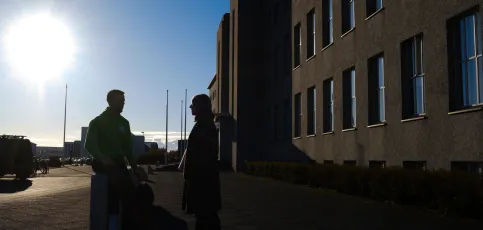 Two people in silhouette in front of main building, sun is shining. 