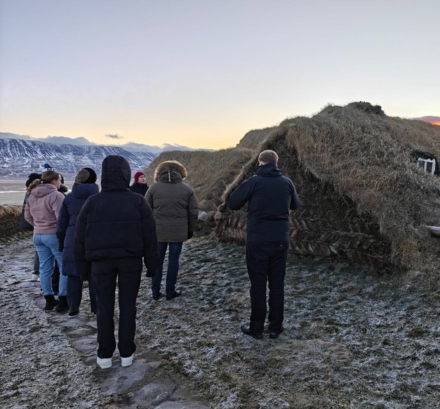 Fólk hlustar á leiðsögumann tala fyrir utan gamlan torfbæ