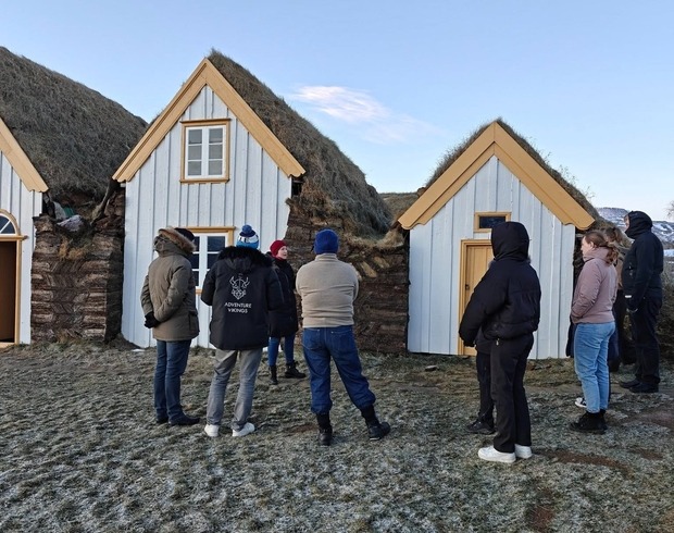 Fólk hlustar á fræðslu fyrir utan gamlan bustabæ