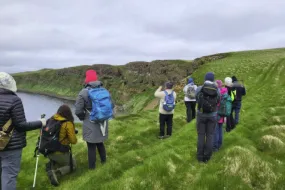 Mynd úr skýrslu, ferðamenn standa í grasi vaxinni hlíð og virða fyrir sér fuglalífið í Hrísey.