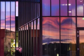 Outside University Centre, at University of Iceland. Sky reflecting in the windows. Woman waving at the camera